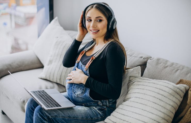 Pregnant woman listening to music in earphones and surfing the internet